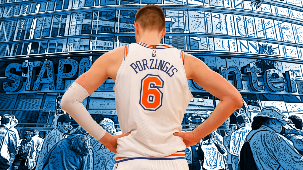 Kristaps Porzingis 穿著紐約尼克隊的球衣，背對著攝影機，站在 Staples Center 前，背景顯示出洛杉磯的球迷和場館標誌。