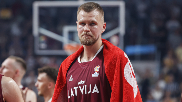 Kristaps Porzingis 穿著拉脫維亞隊球衣，沮喪地坐在場邊，顯示出比賽中的失落情緒。